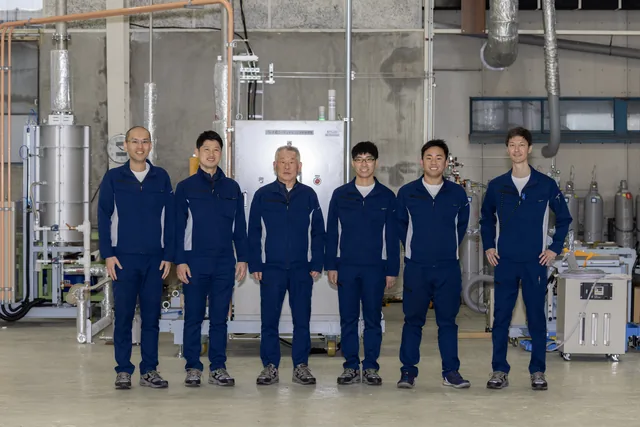 Members at the Gifu plant. Eight people in work clothes standing in front of the production line.